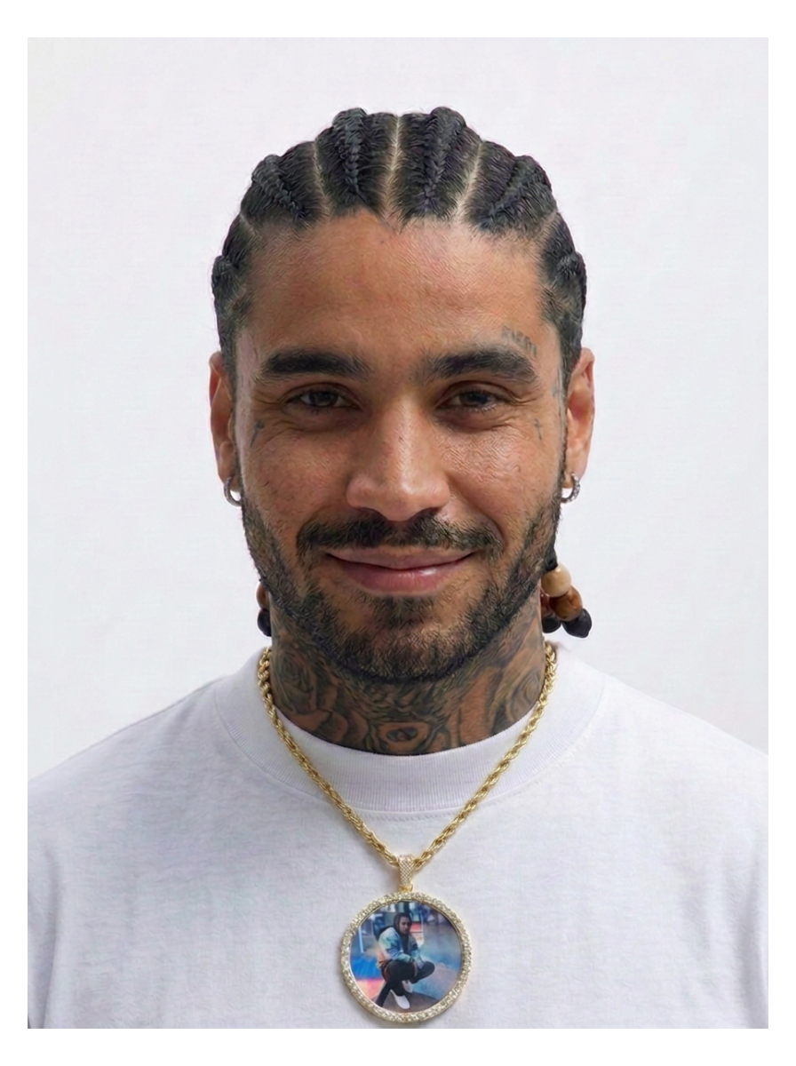 A man with braided hair and neck tattoos wearing a white t-shirt and a gold chain necklace with a custom oval photo pendant, set against a plain white background.